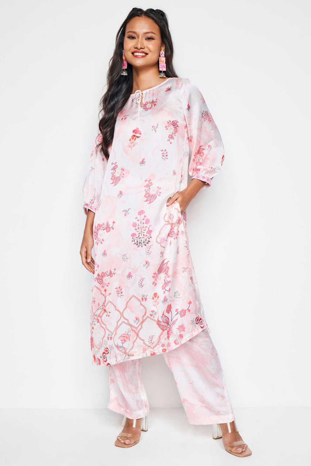 Woman wearing a pink floral kurta with white pants on a white background