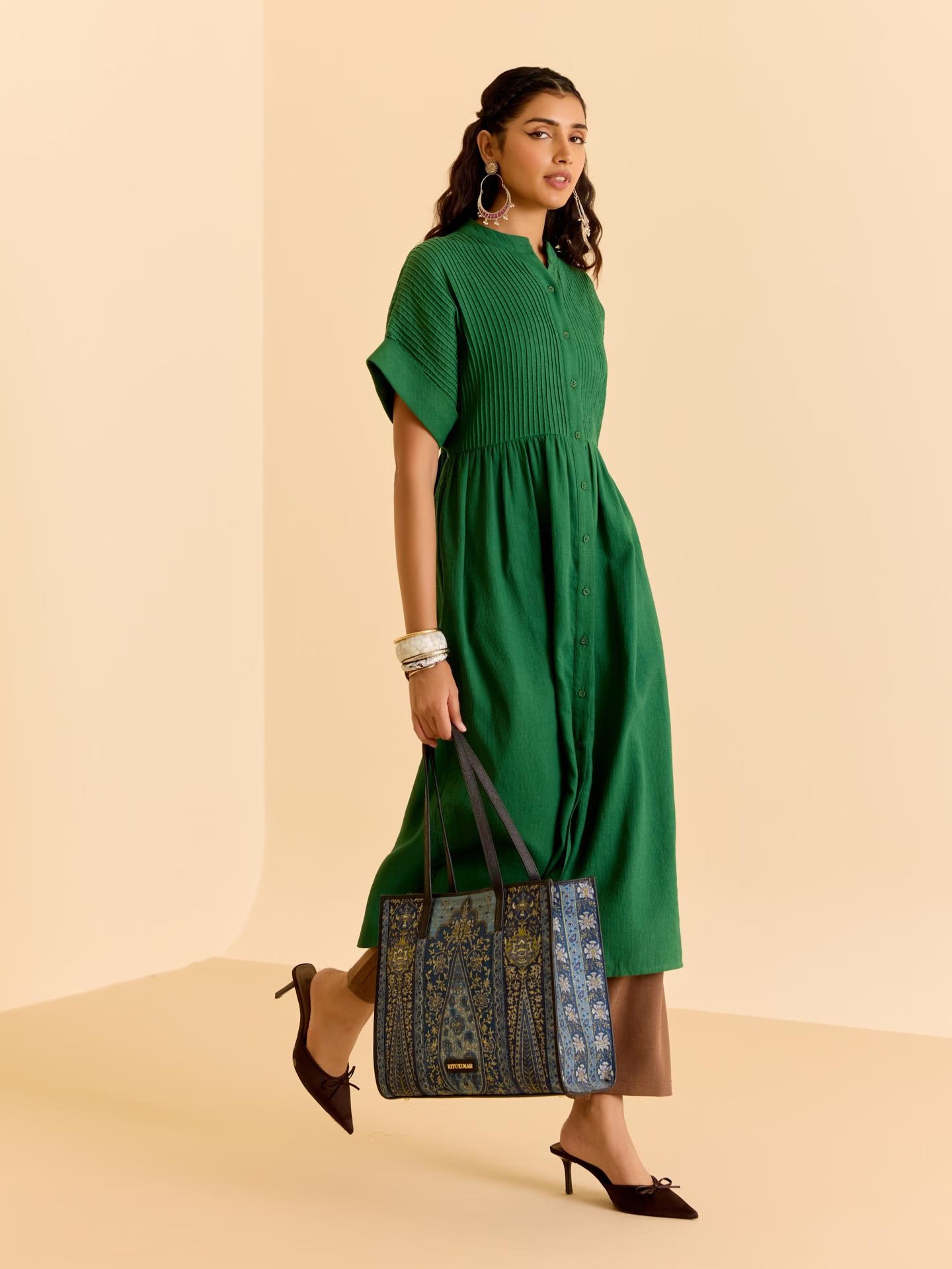 Woman in a green dress holding a patterned bag on a beige background