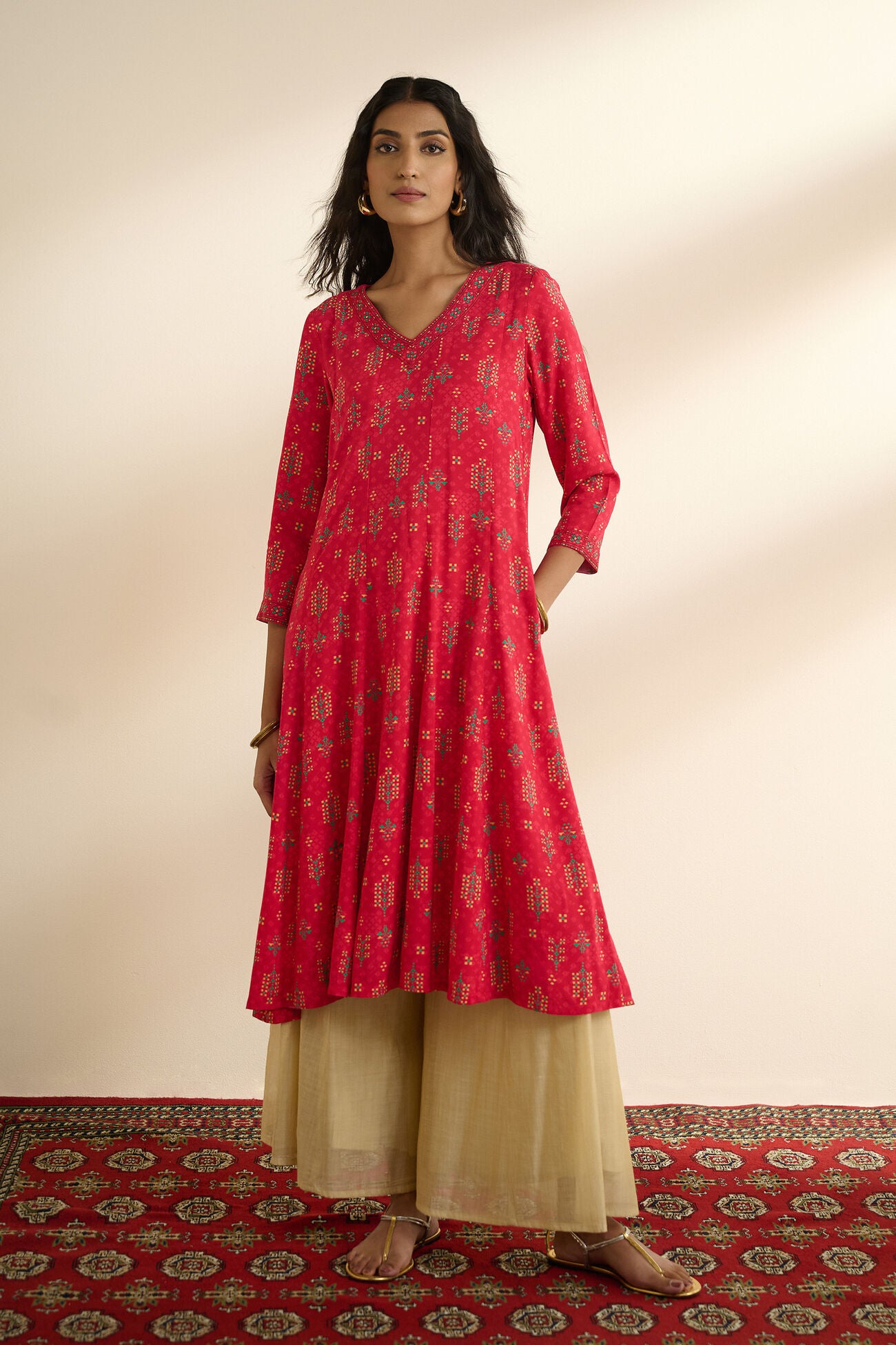 Woman wearing a red patterned kurta with beige palazzo pants on a neutral background