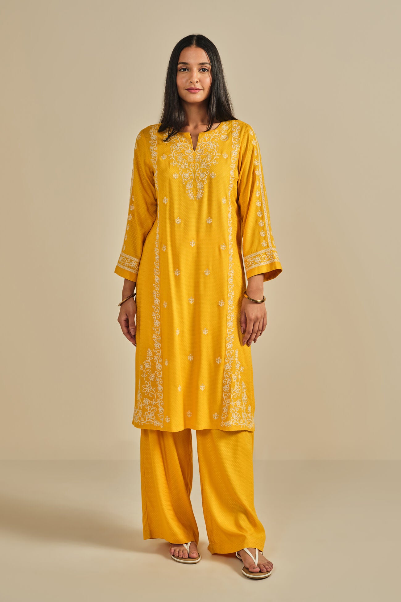 Woman wearing a yellow embroidered kurta with palazzo pants on a beige background