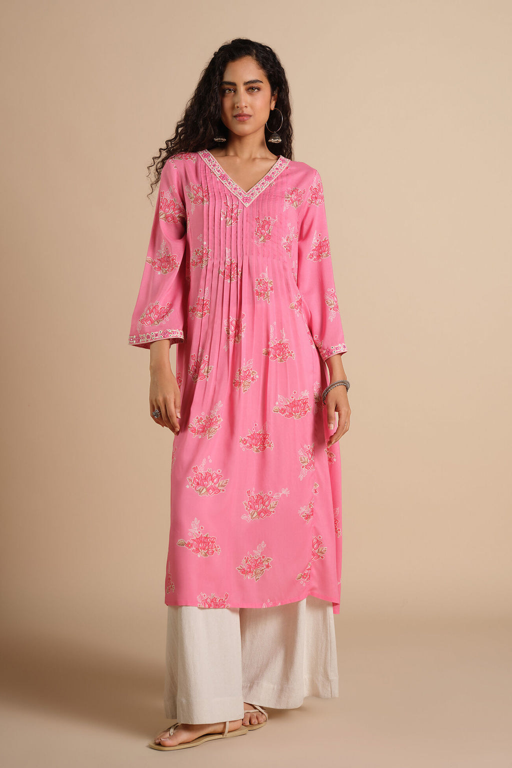 Woman wearing a pink floral kurta with white pants on a beige background