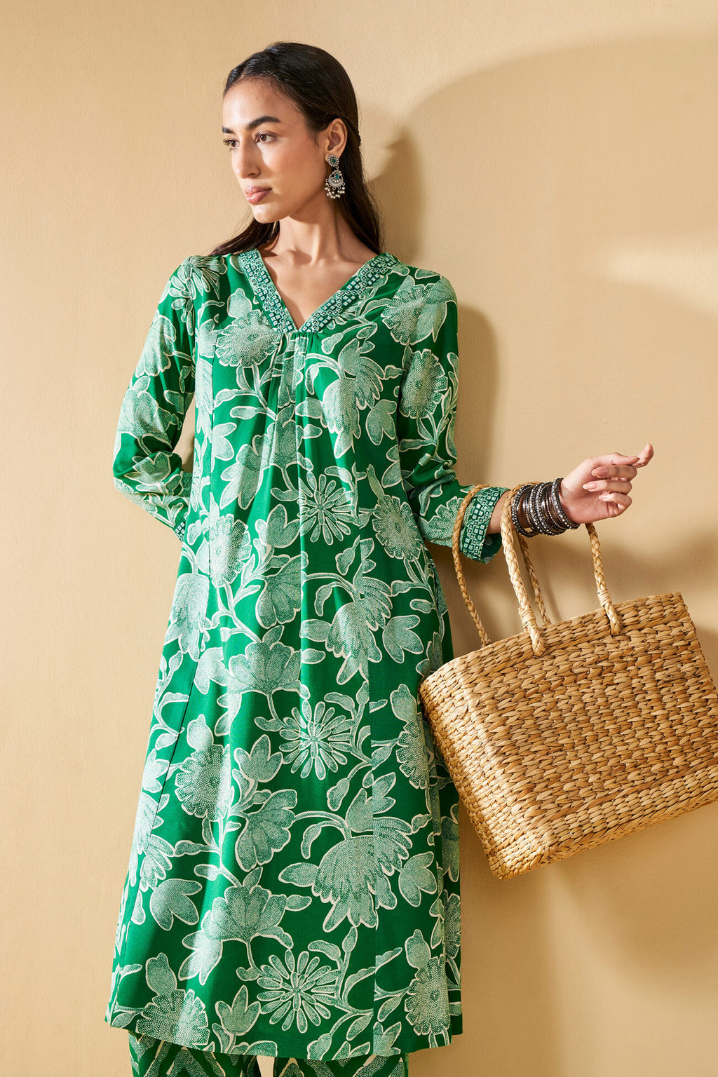 Woman in a green floral dress holding a woven bag against a beige background
