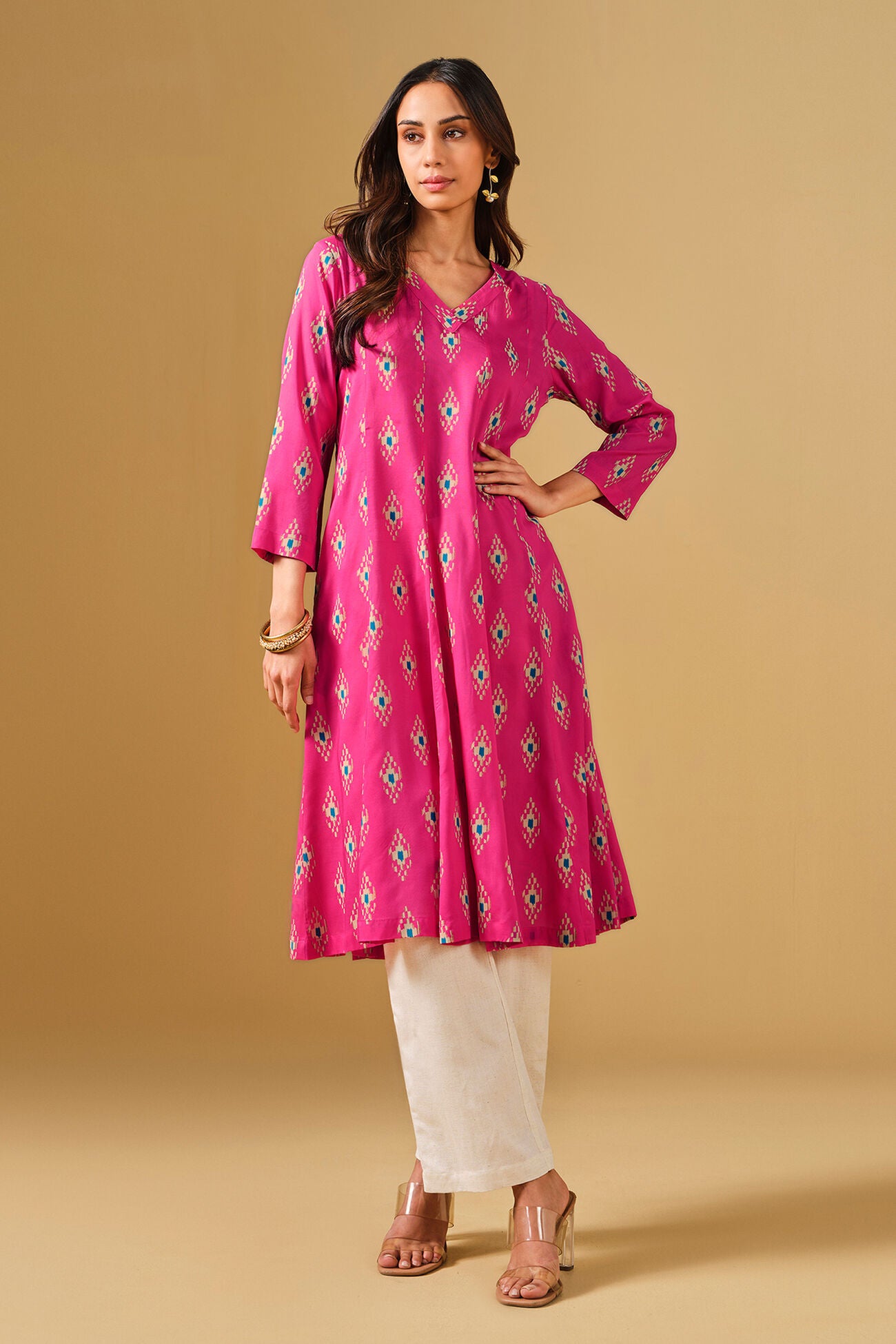 Woman wearing a pink patterned kurta with white pants on a beige background