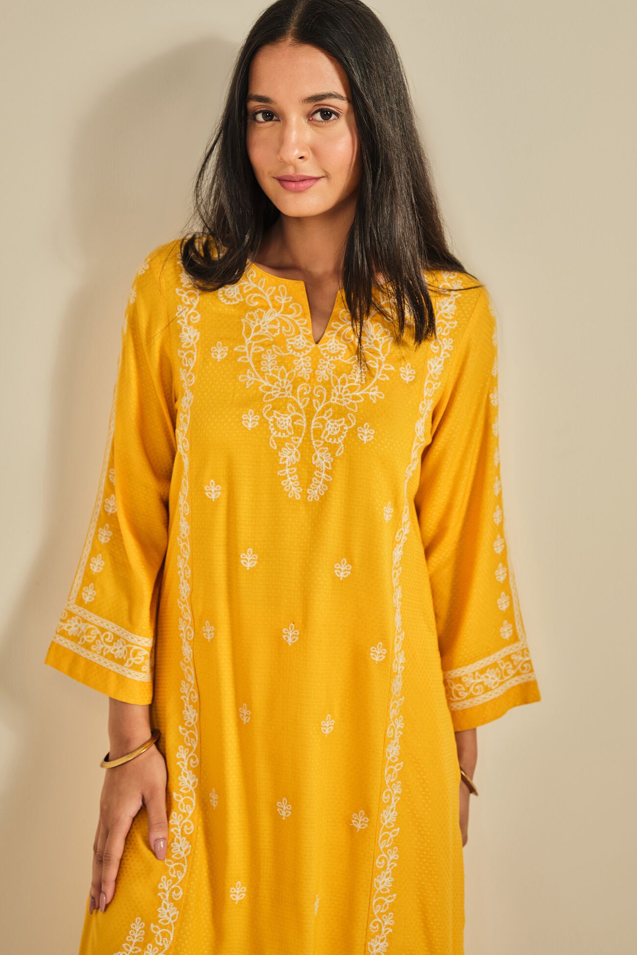 Woman wearing a yellow embroidered kurta against a beige background