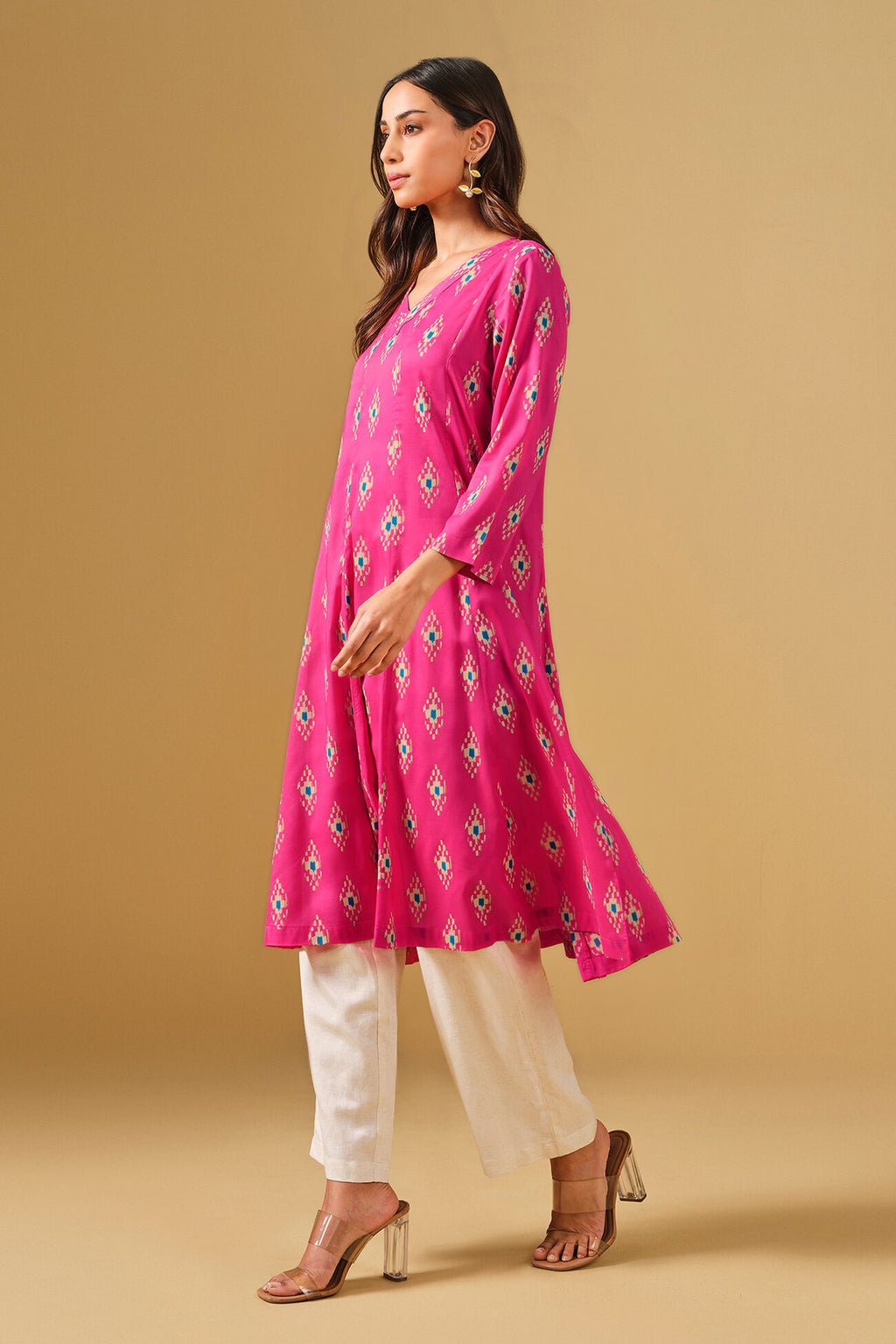 Woman wearing a pink floral kurta with white pants on a beige background