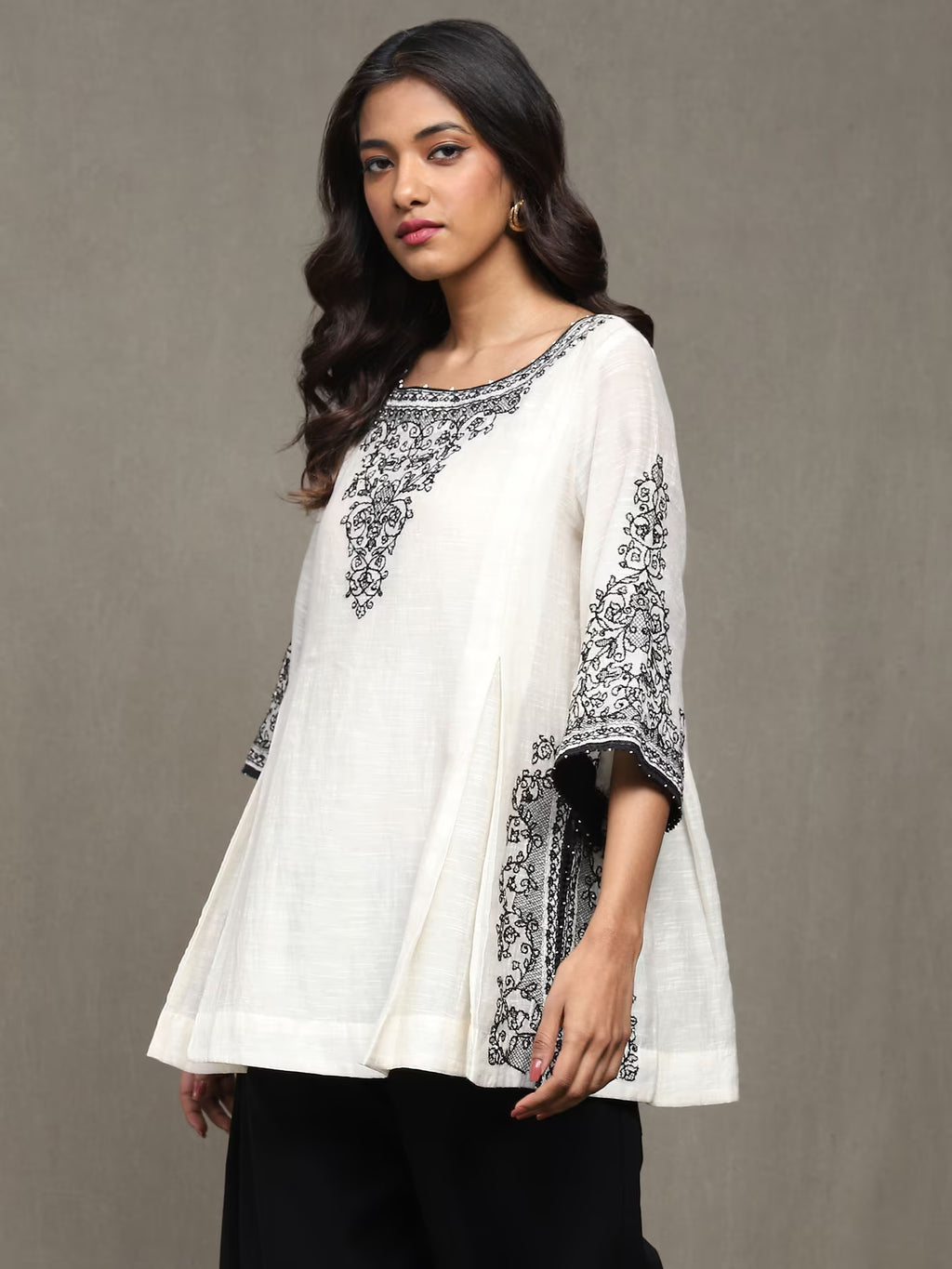 Woman wearing a white top with black embroidery against a gray background