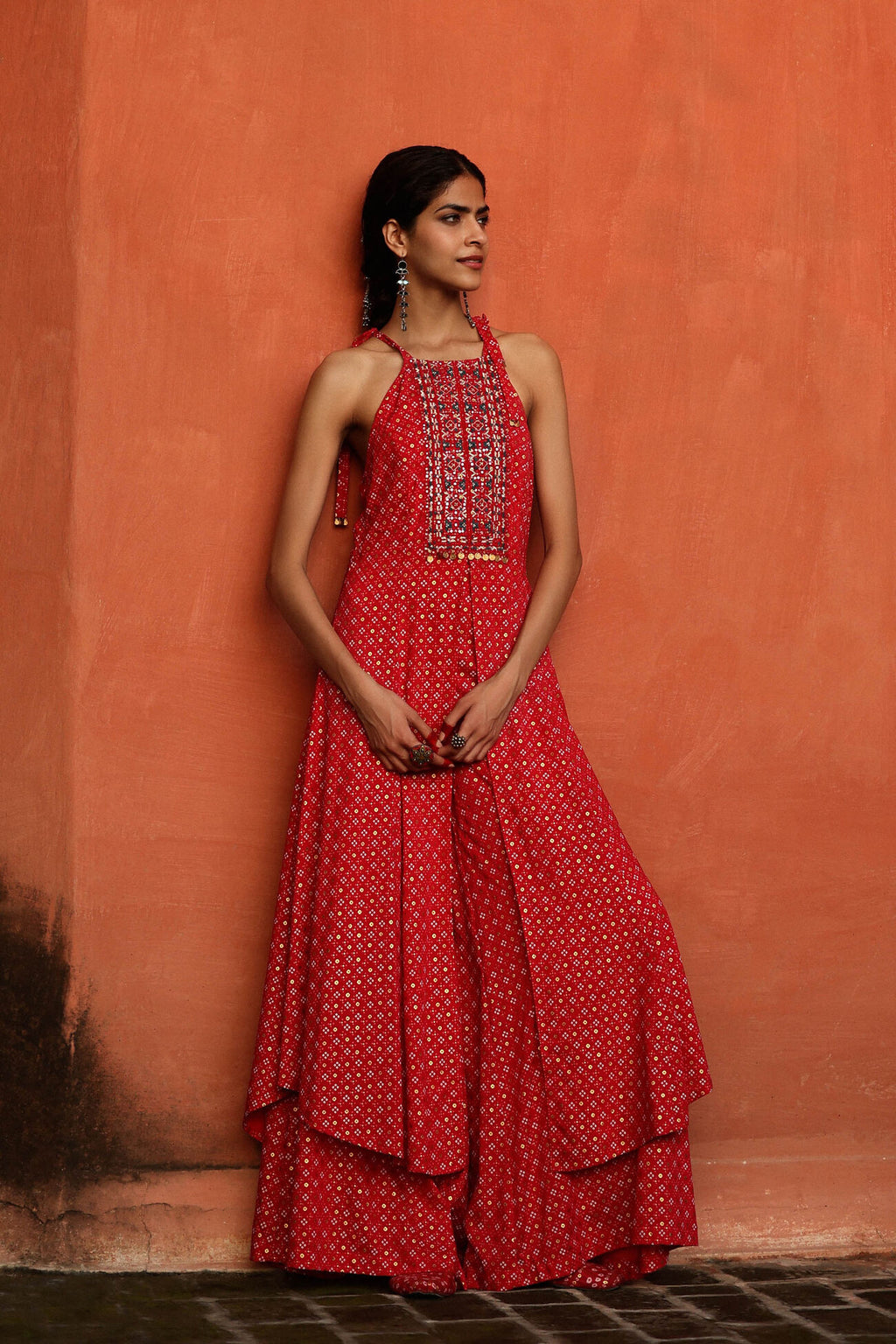 Woman wearing a red dress with white patterns against an orange wall.