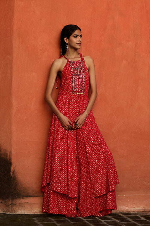 Woman wearing a red dress with white patterns against an orange wall.