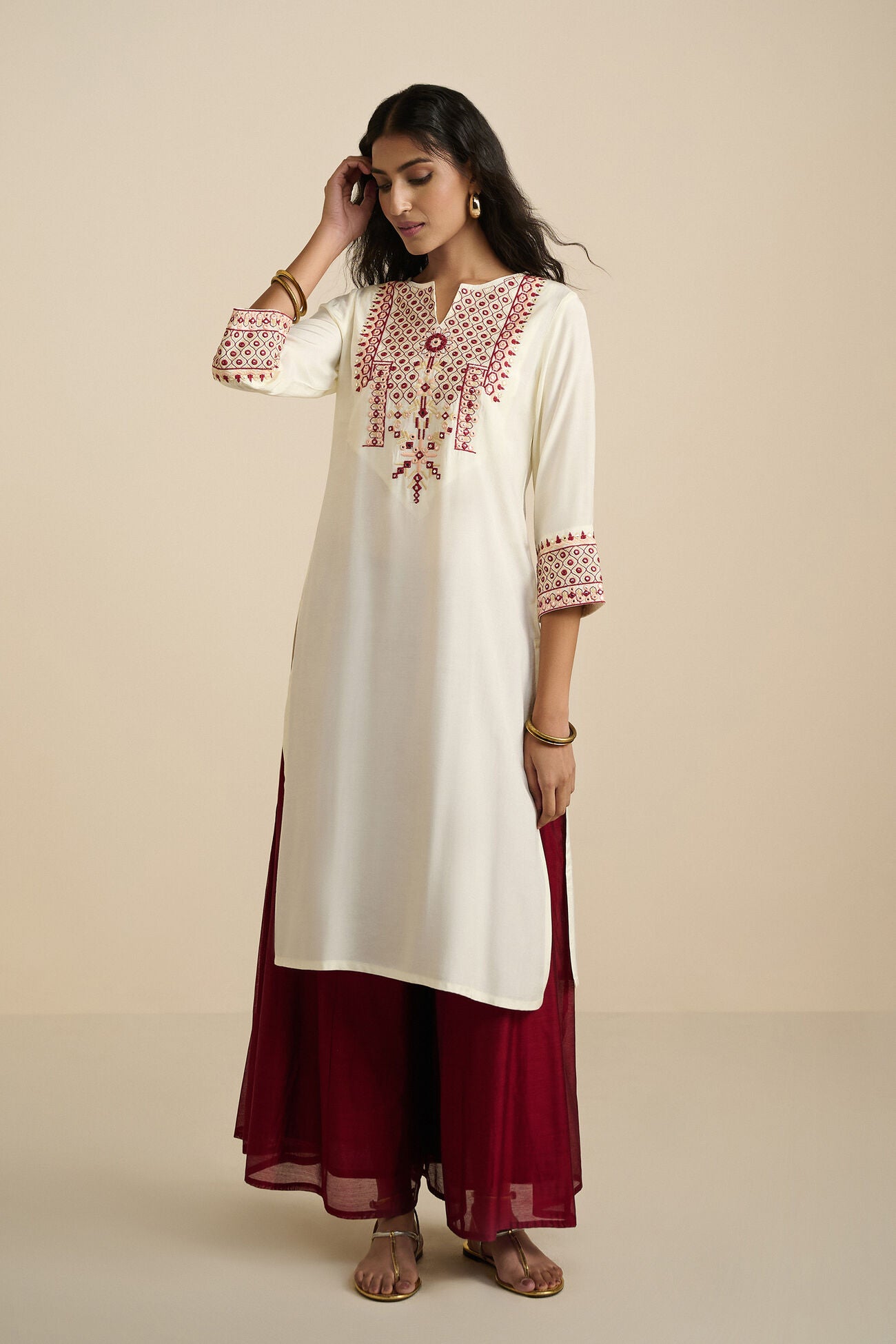 Woman wearing a white kurta with red embroidery and maroon pants on a beige background