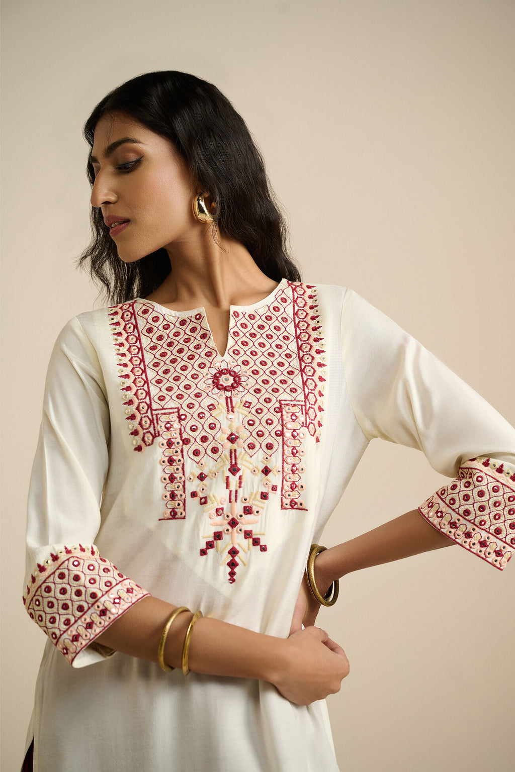 Woman wearing a white kurta with red embroidery on a beige background