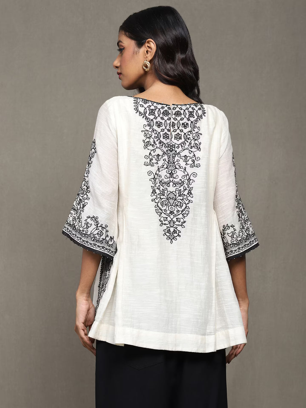 Woman wearing a white top with black embroidery on a gray background