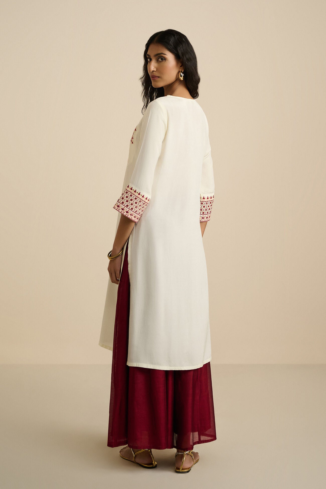 Woman wearing a white kurta with red bottom and red embroidery on a beige background