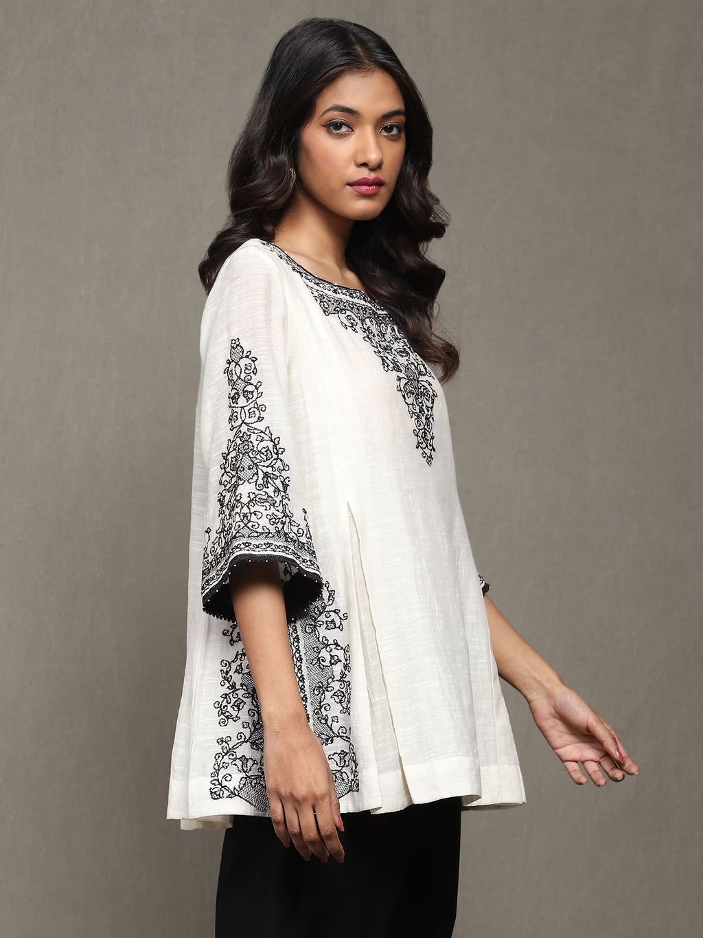 Woman wearing a white top with black embroidery against a gray background