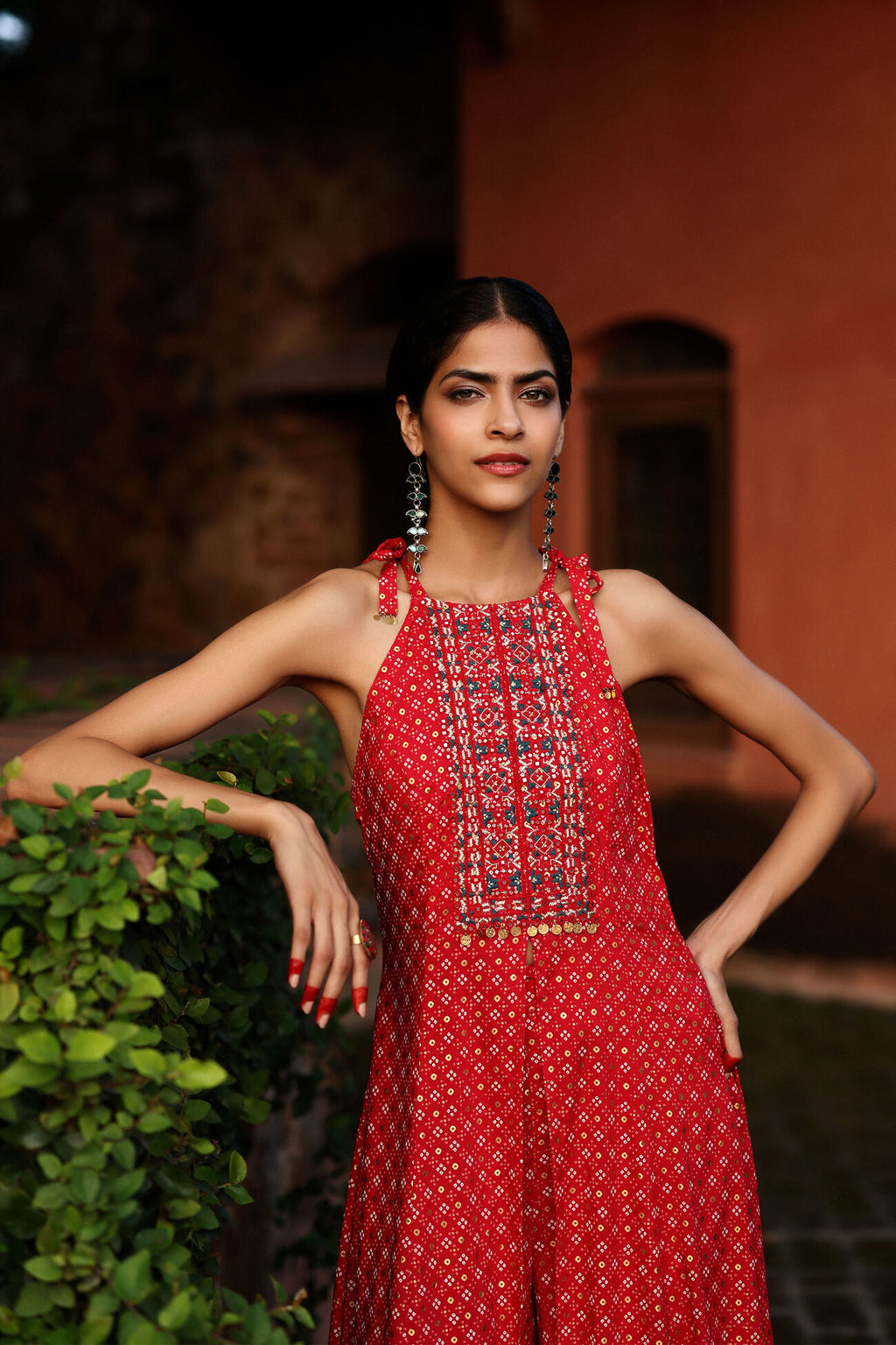 Woman in a red dress with intricate detailing standing outdoors.