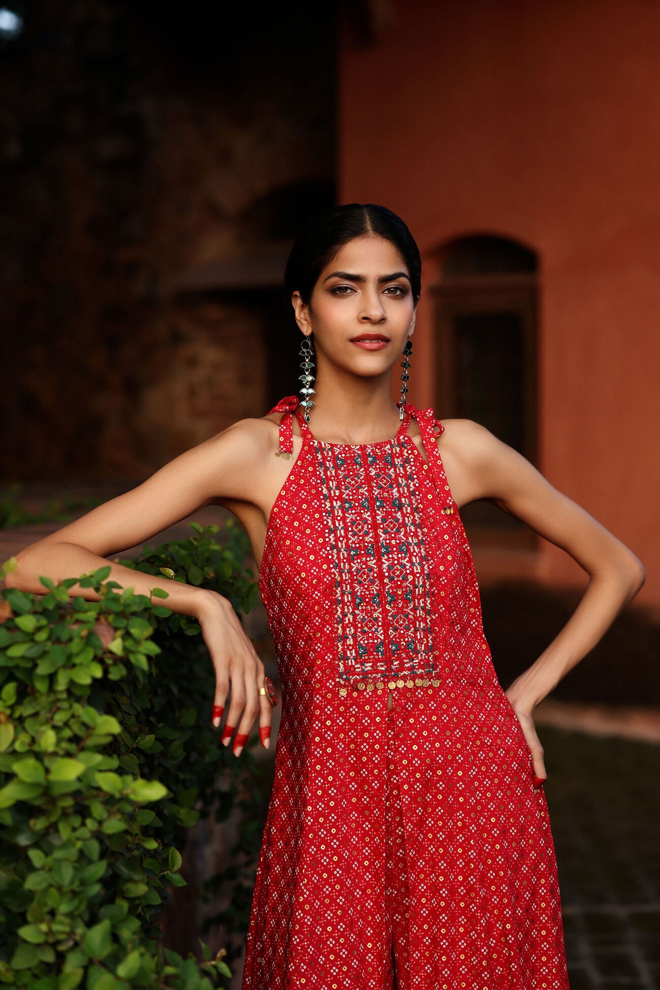 Woman in a red dress with intricate detailing standing outdoors.