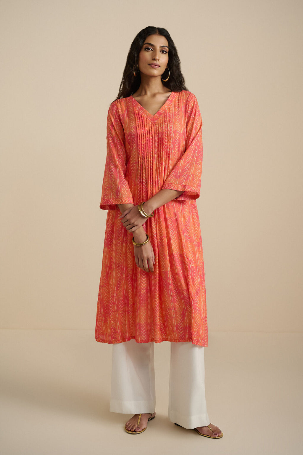 Woman wearing a red and orange patterned kurta with white pants on a beige background