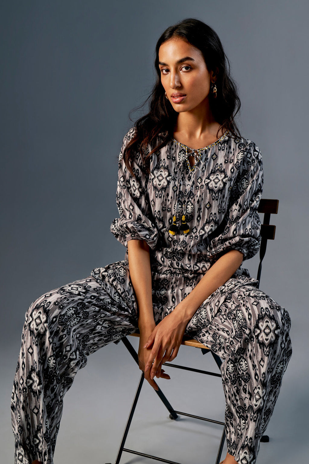 Woman sitting on a chair wearing a patterned outfit against a gray background