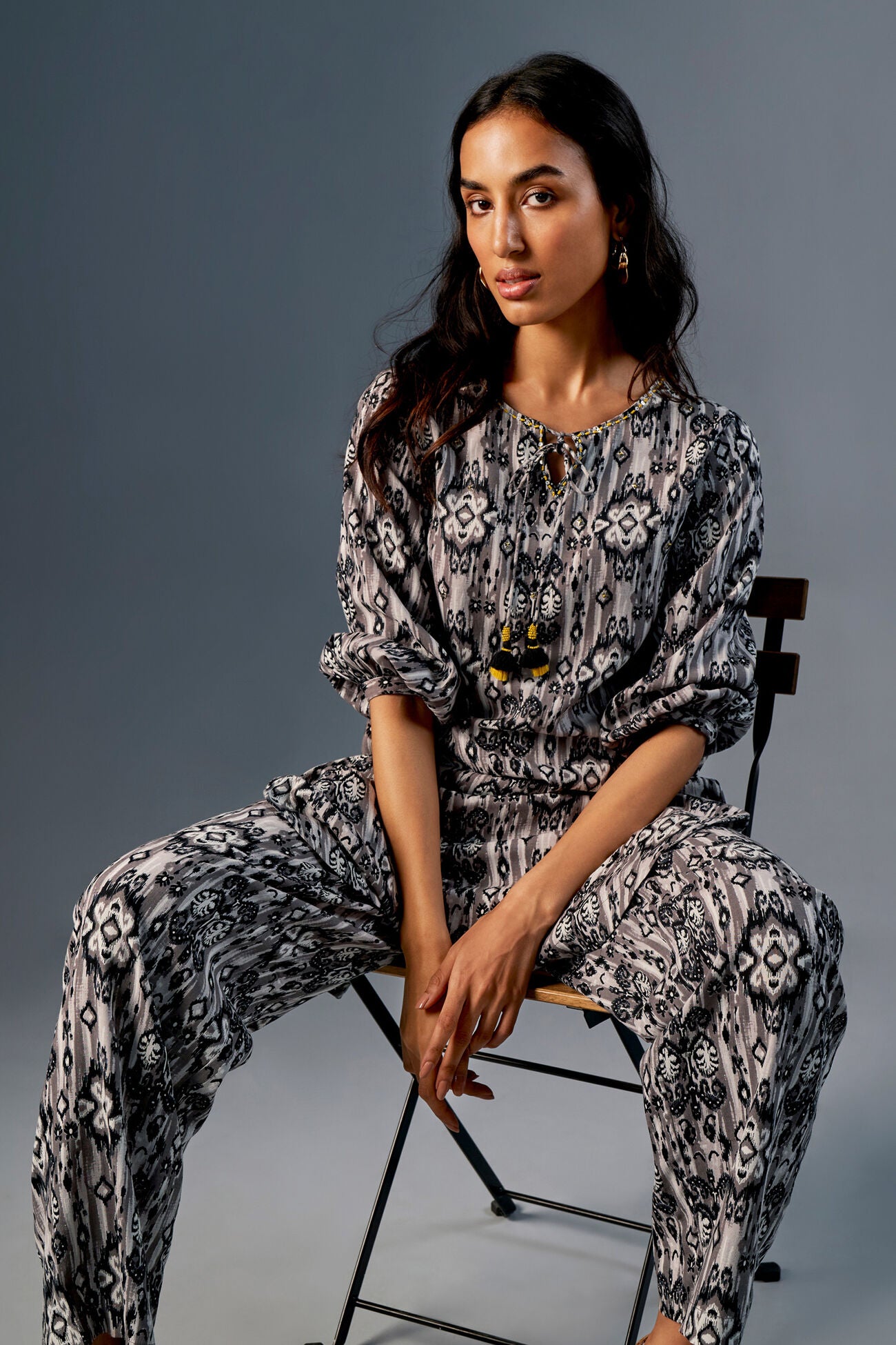 Woman sitting on a chair wearing a patterned outfit against a gray background