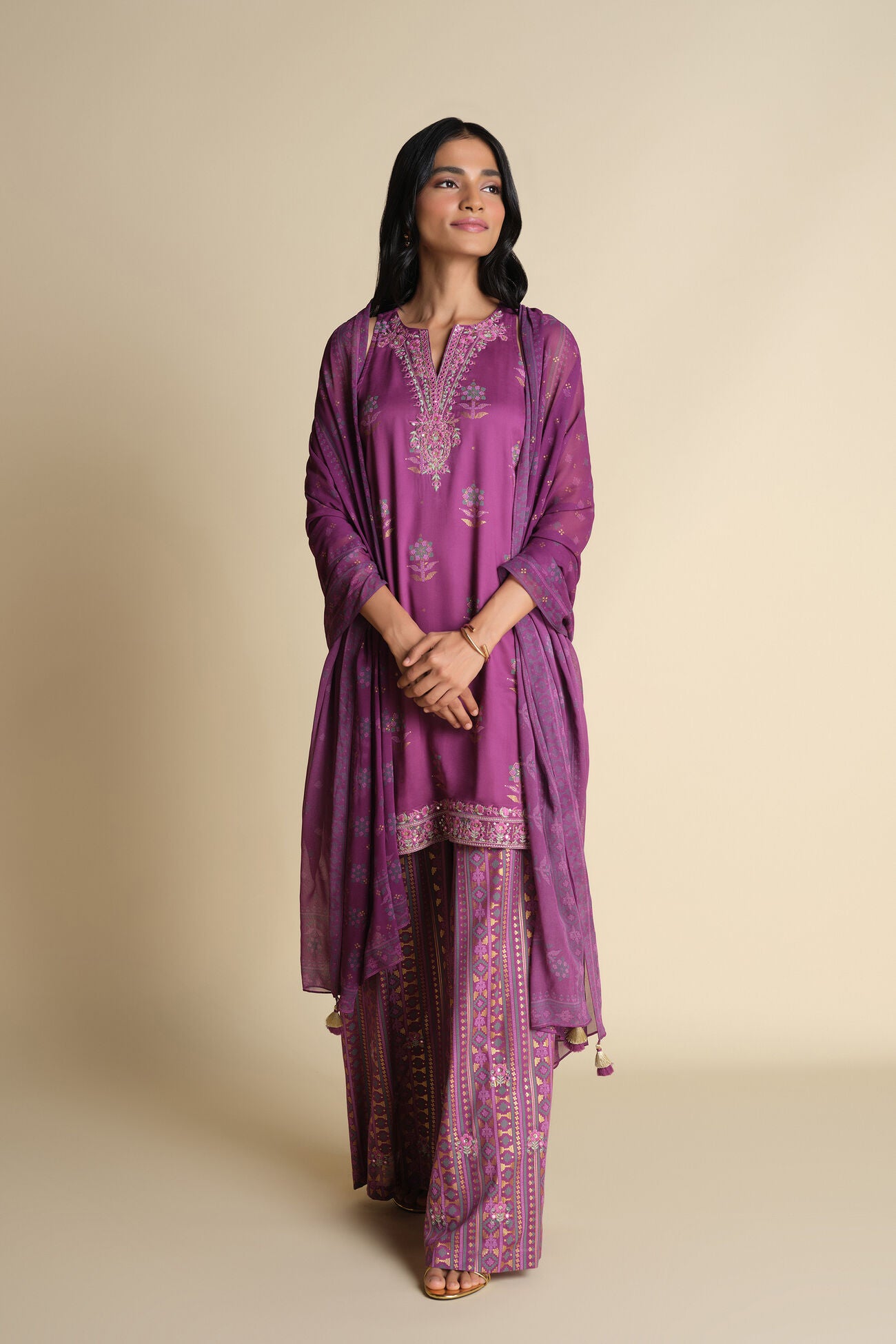 Woman wearing a purple traditional outfit with intricate patterns on a beige background