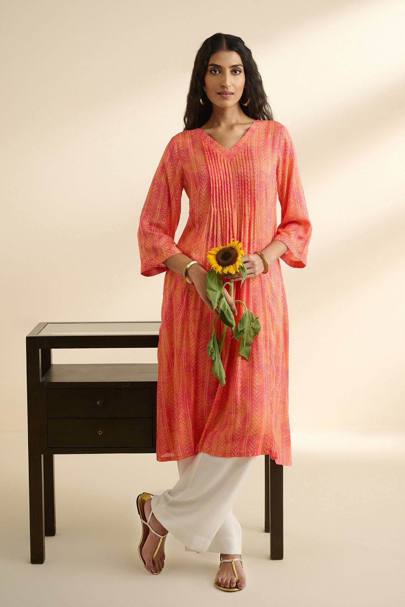 Woman in a pink and orange striped kurta holding a sunflower against a plain background