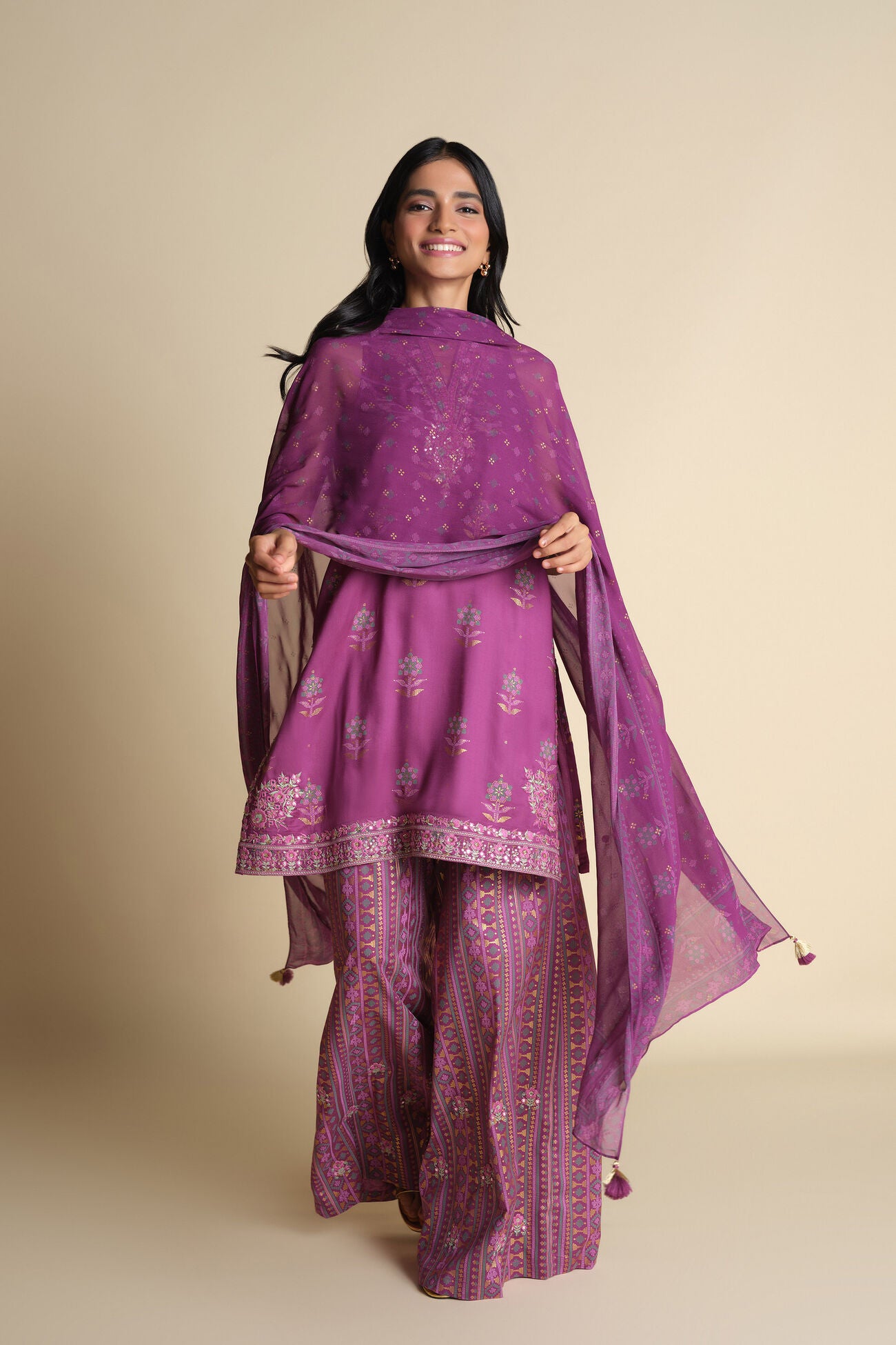 Woman wearing a purple traditional outfit with a matching dupatta on a beige background