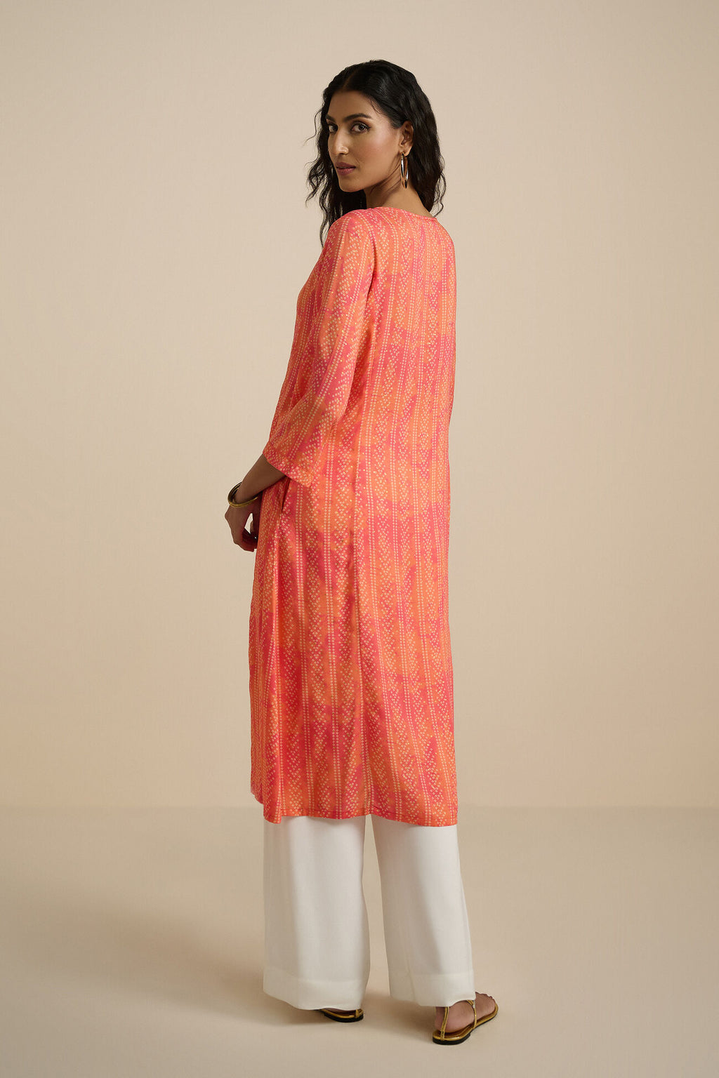 Woman wearing a pink and orange checkered kurta with white pants on a beige background