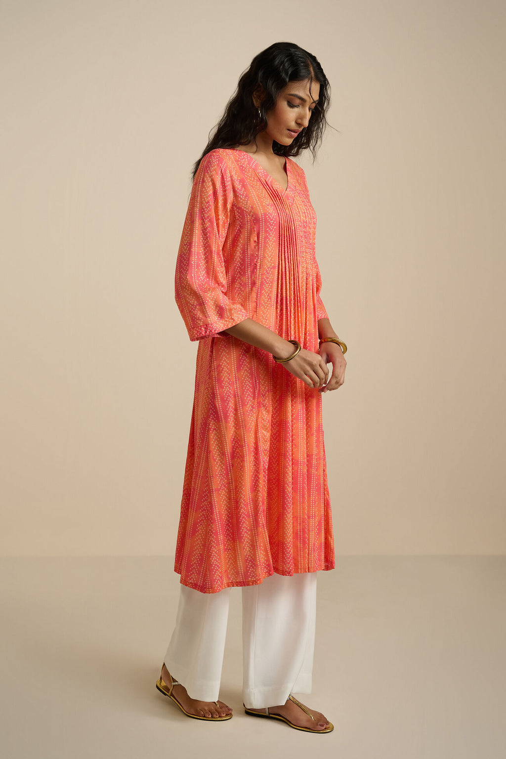 Woman wearing an orange and pink tie-dye kurta with white pants on a beige background