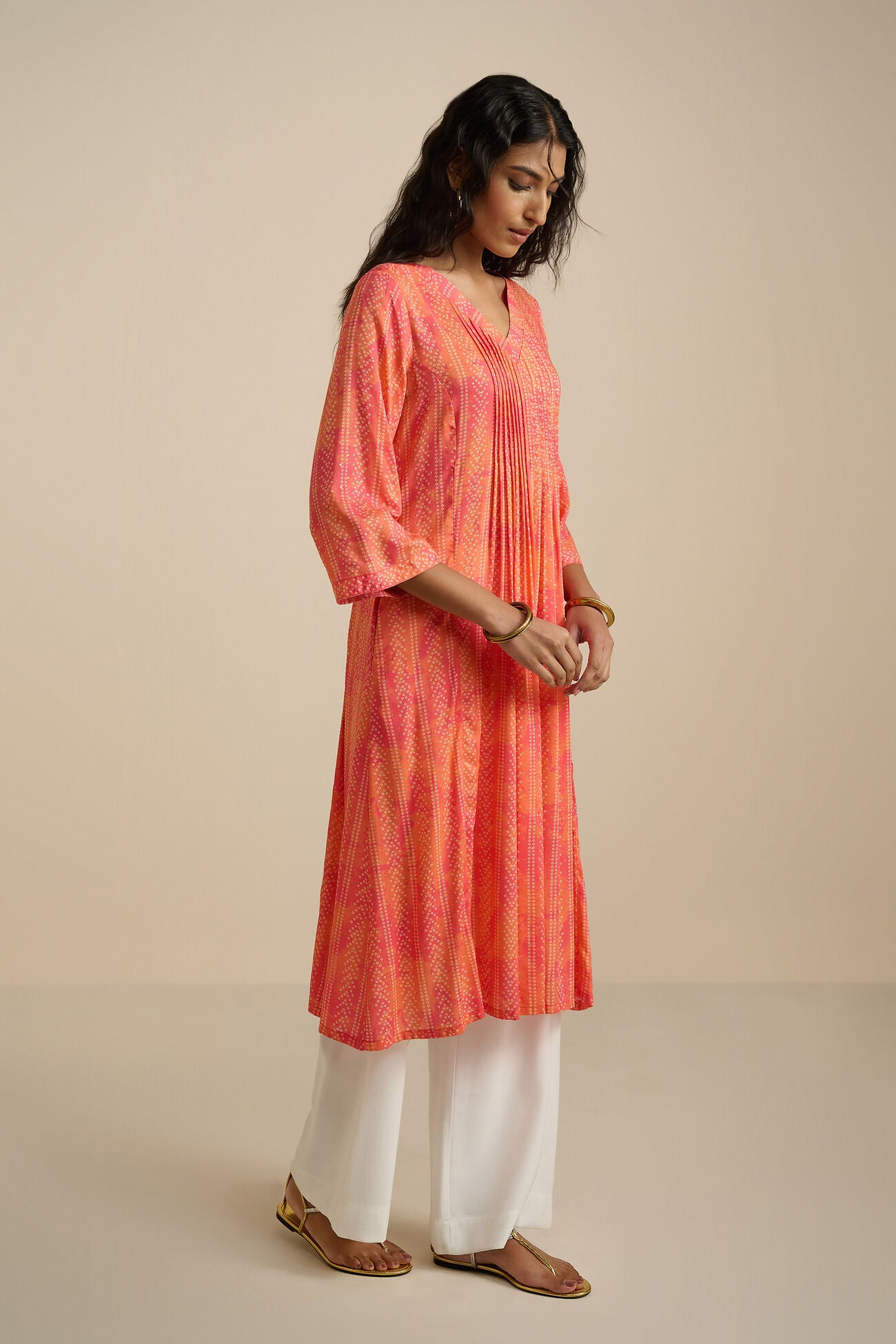 Woman wearing an orange and pink tie-dye kurta with white pants on a beige background