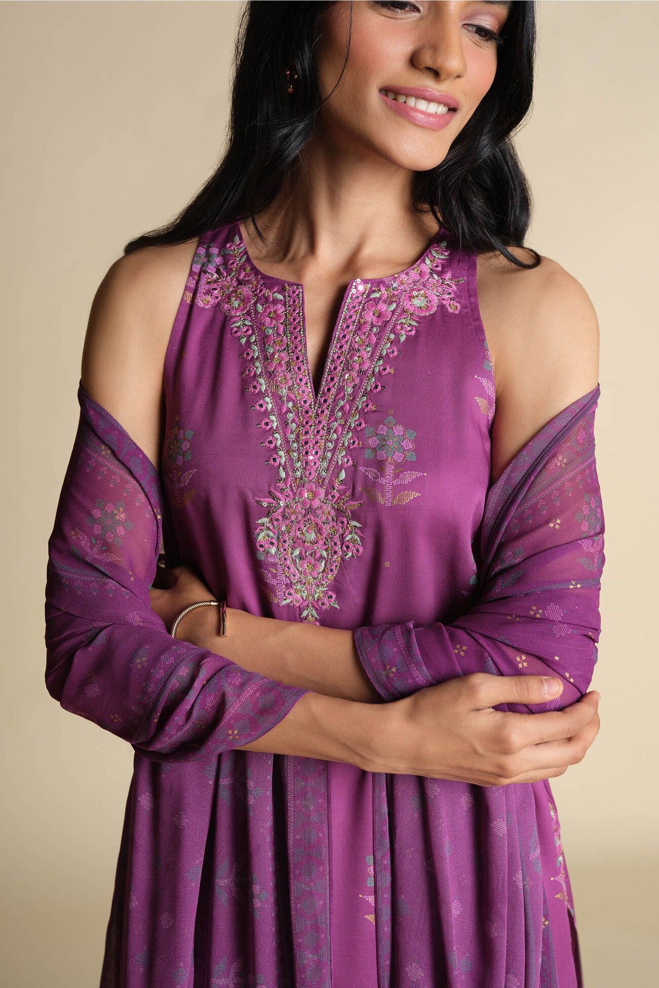 Woman wearing a purple embroidered dress with sheer sleeves against a beige background