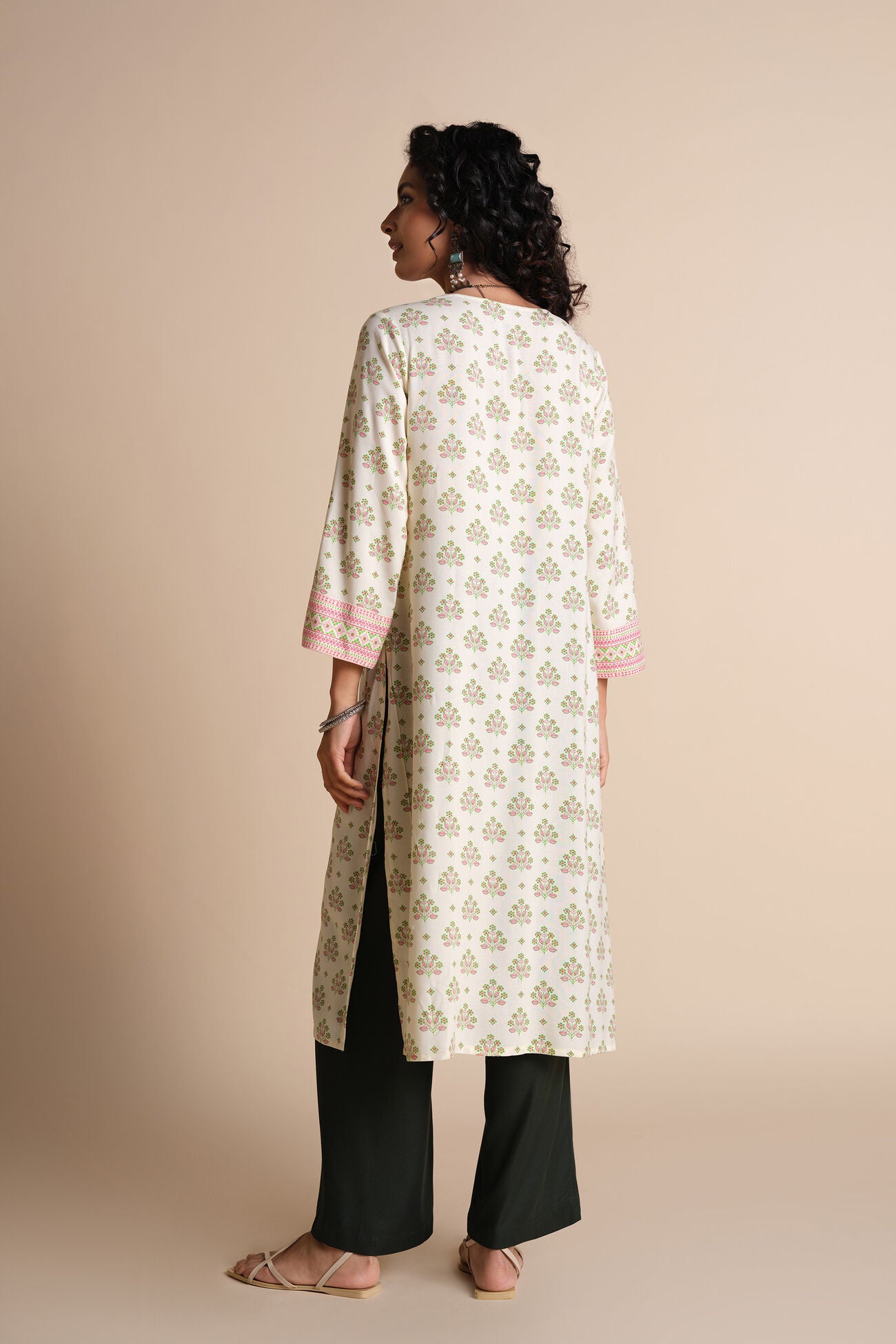 Woman wearing a long, light-colored floral patterned kurta with black pants on a beige background