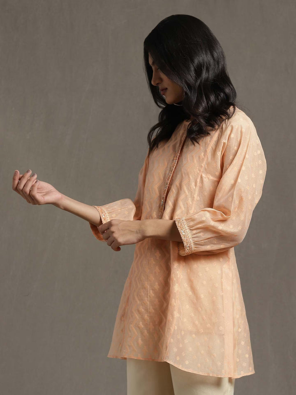 Woman wearing a peach-colored kurta with intricate patterns against a gray background