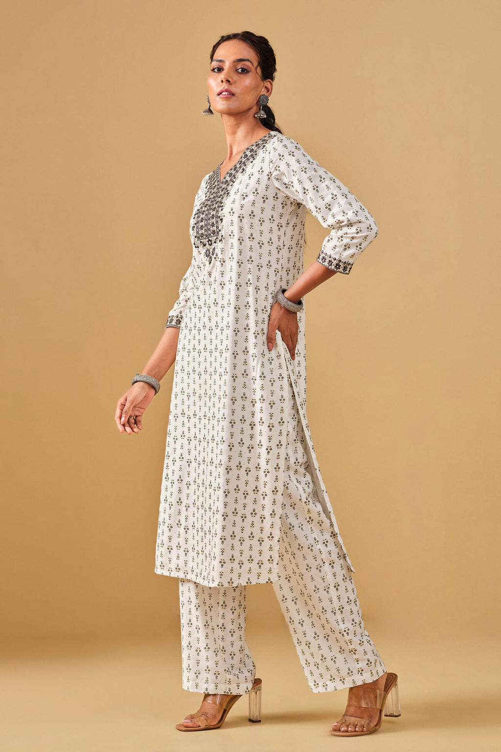 Woman wearing a white floral kurta with matching pants on a beige background