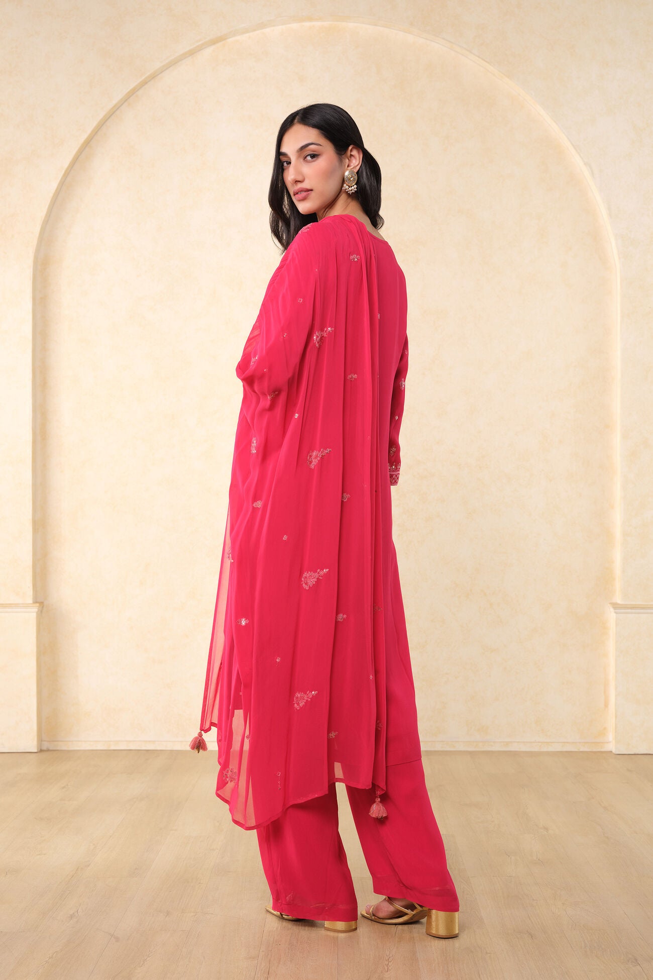Woman wearing a pink traditional outfit with a matching dupatta against a beige wall.