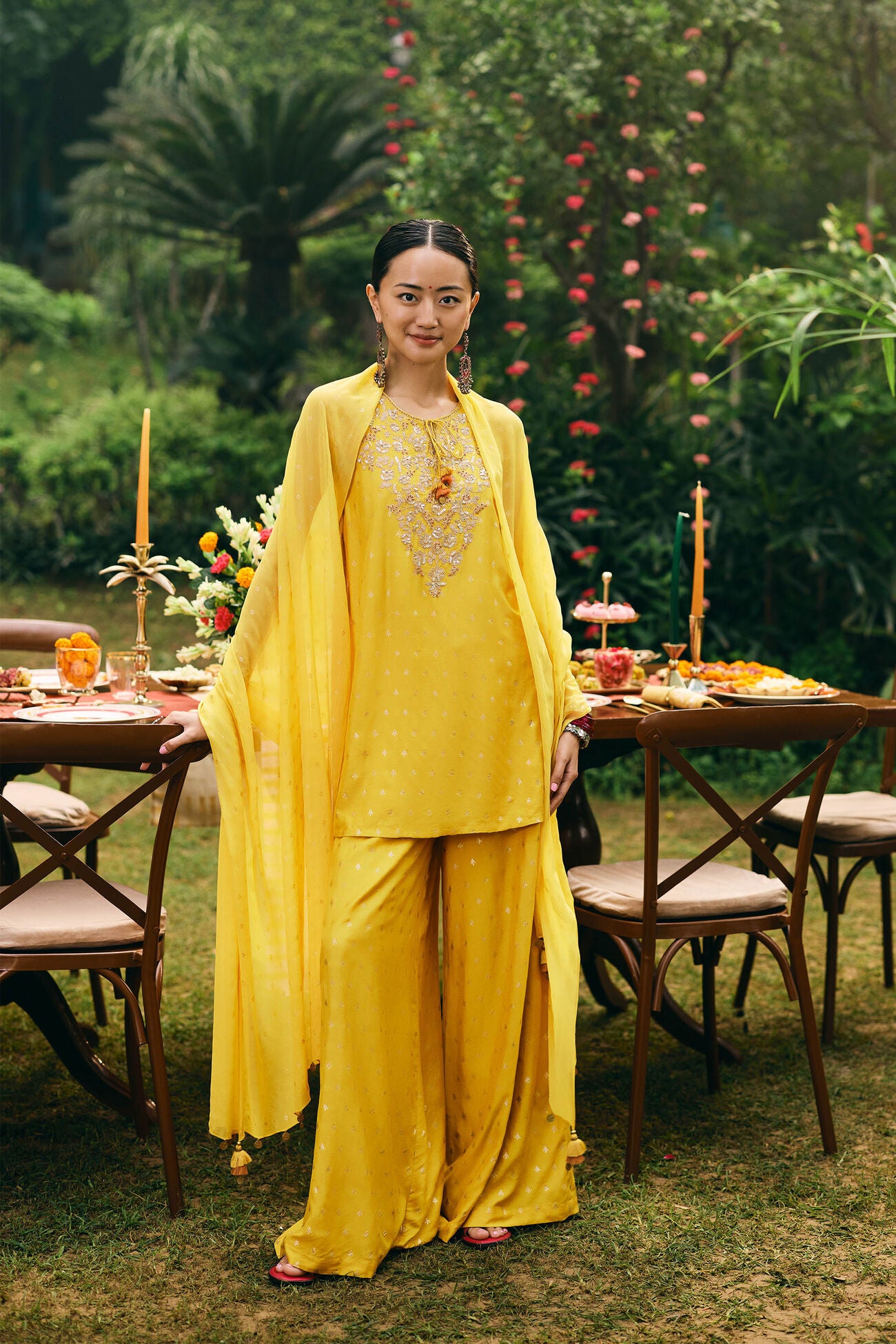 Woman in a yellow outfit standing in a garden with tables and floral arrangements.