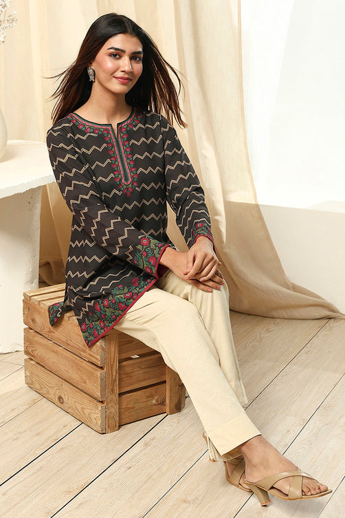 Woman sitting on a wooden crate wearing a black and red patterned top with beige pants.