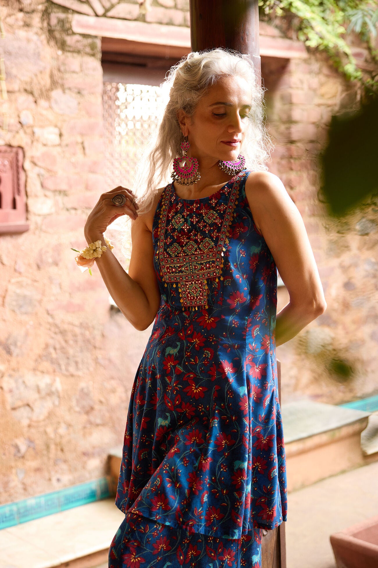 Woman wearing a blue floral dress with intricate detailing in an outdoor setting.