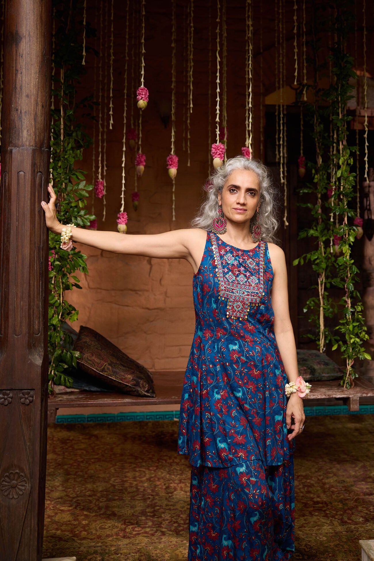 Woman in a blue floral dress standing in a decorated indoor setting with hanging decorations and plants.