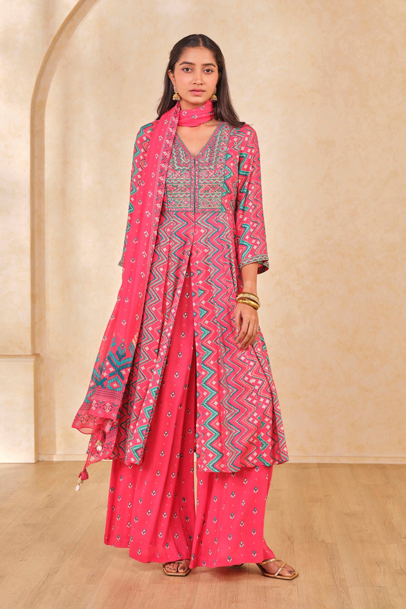 Woman wearing a pink traditional outfit with a matching dupatta against a beige background