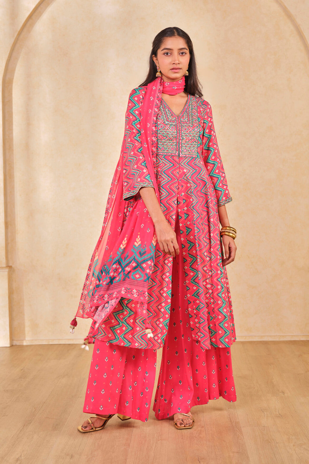 Woman wearing a pink traditional outfit with a matching dupatta against a beige wall.
