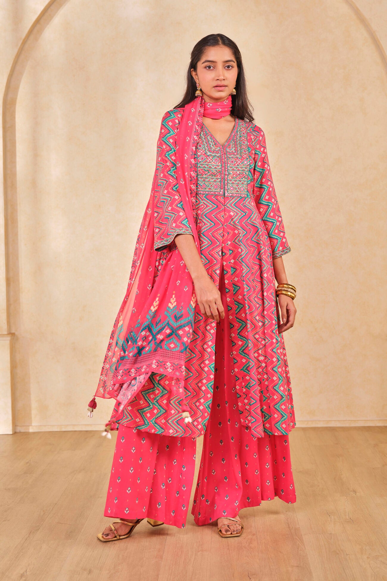 Woman wearing a pink traditional outfit with a matching dupatta against a beige wall.