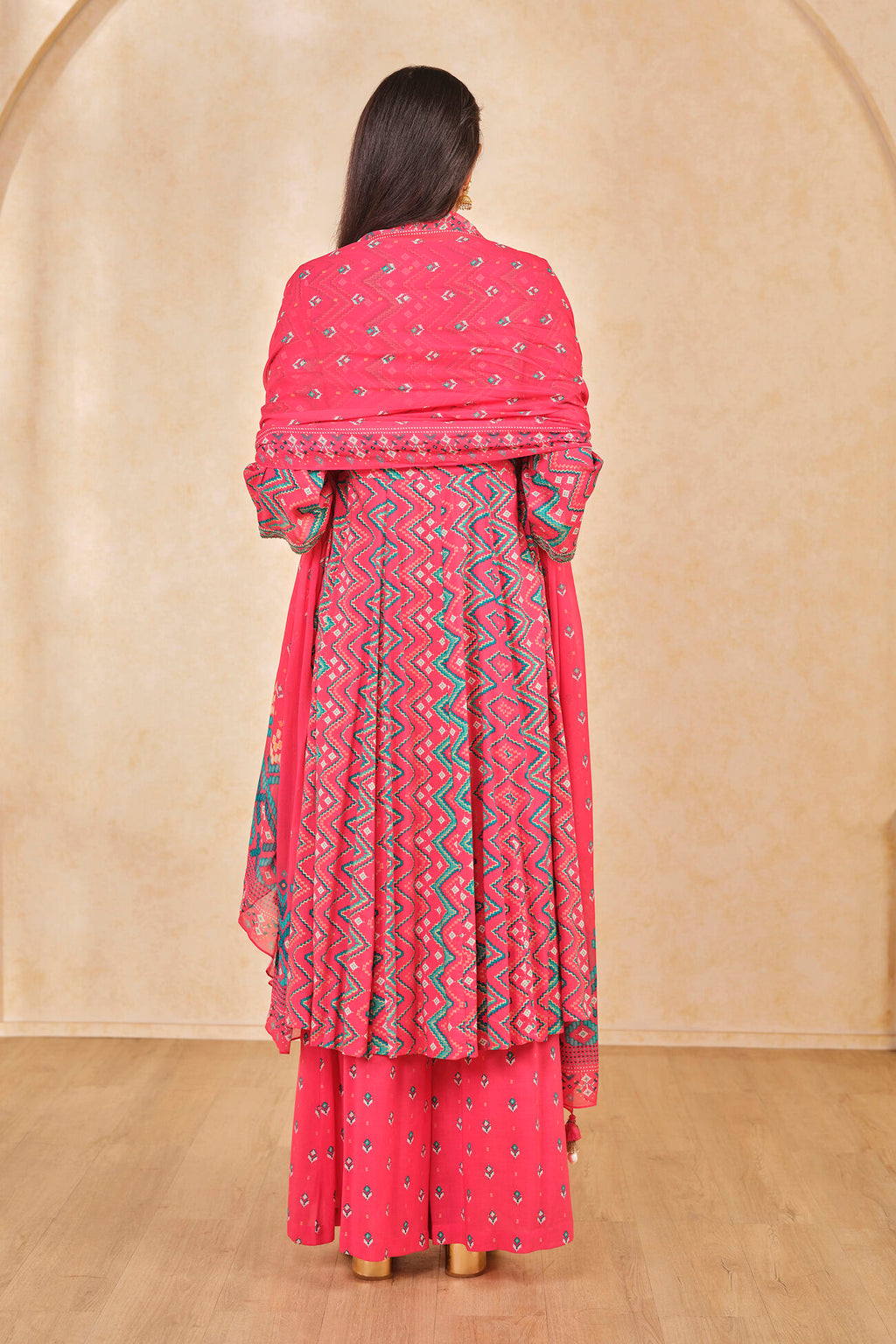 Woman wearing a pink traditional outfit with a matching dupatta against a beige background