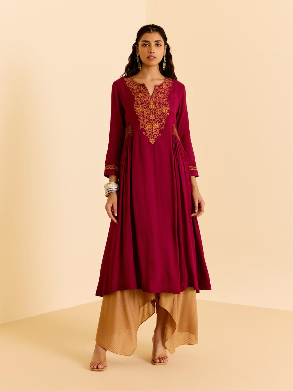 Woman wearing a maroon dress with gold embroidery on a beige background