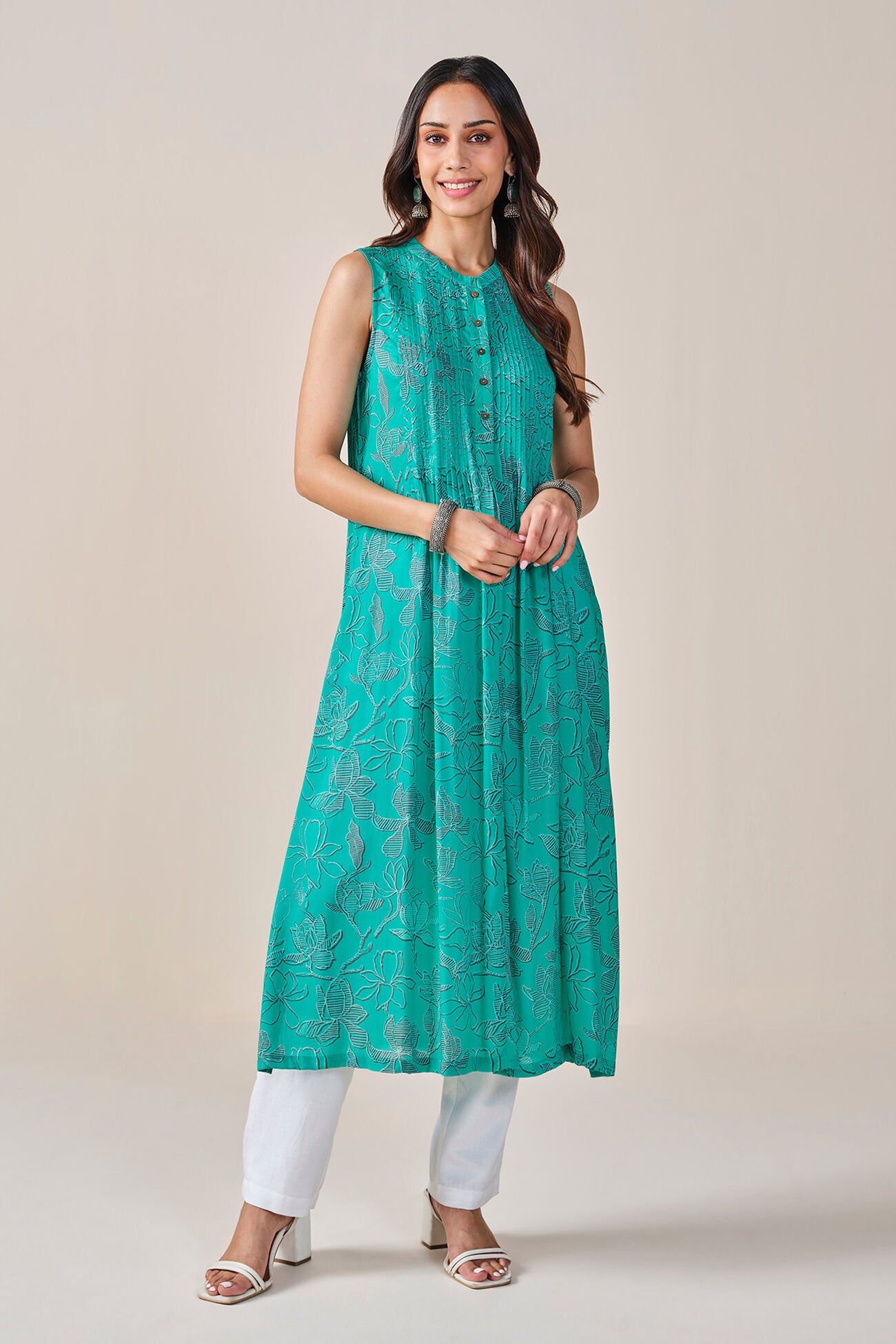 Woman wearing a teal sleeveless kurta with white pants on a beige background