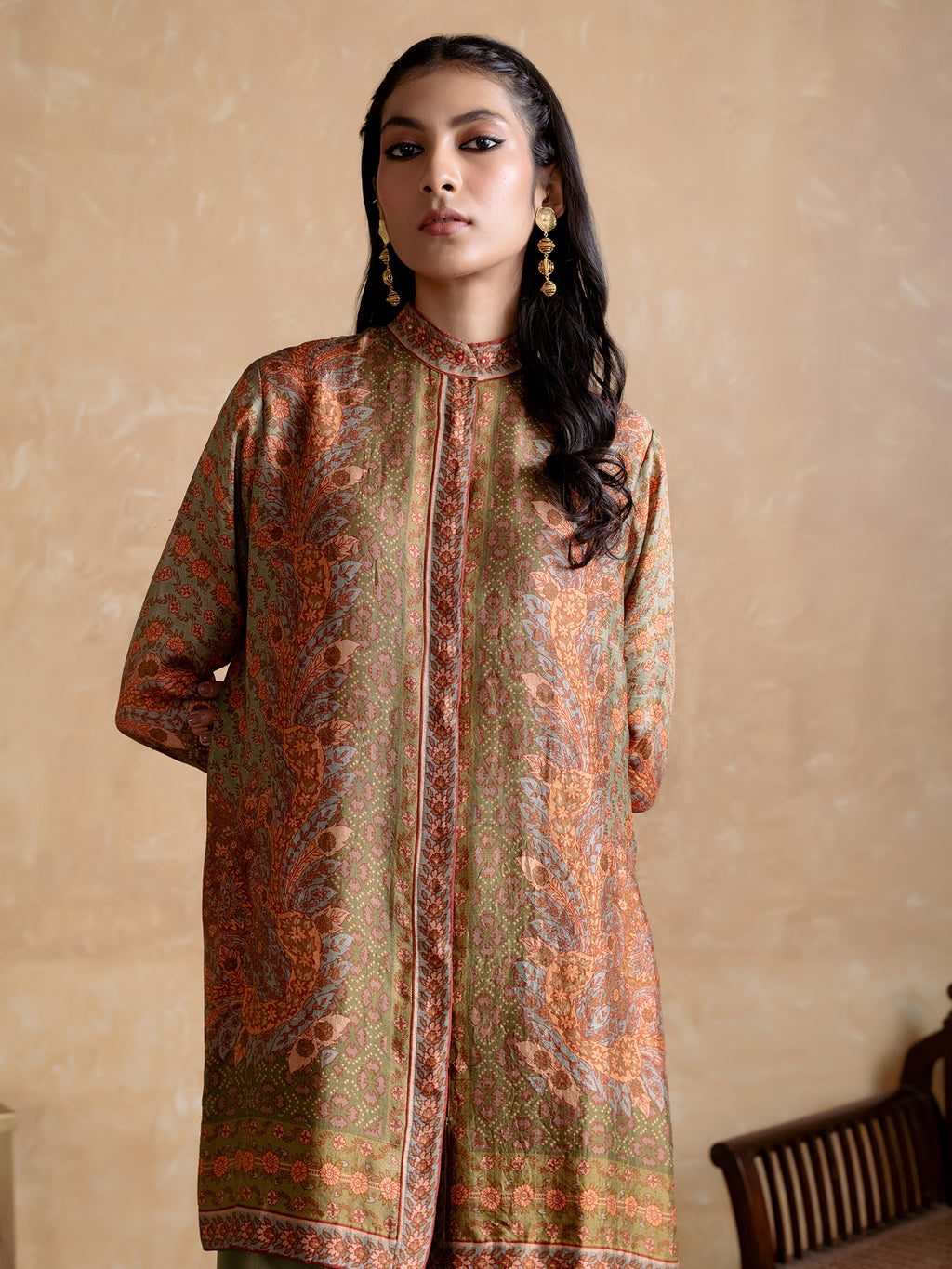 Woman wearing a patterned long shirt against a beige wall