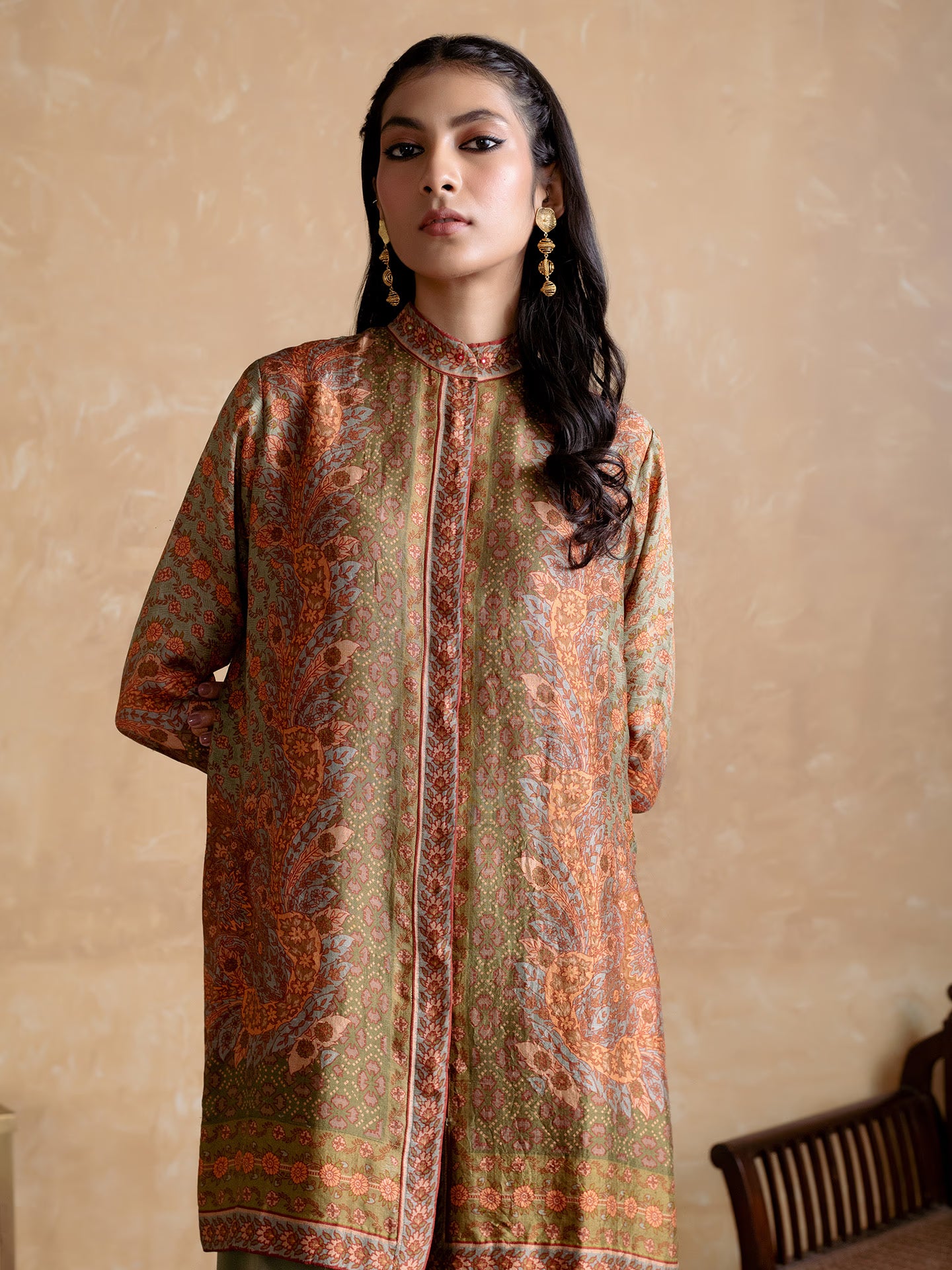 Woman wearing a patterned long shirt against a beige wall