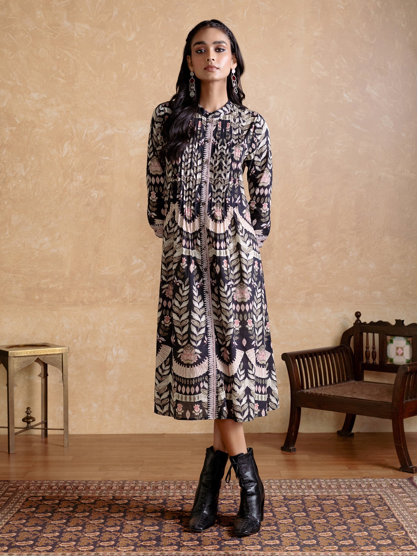 Woman wearing a patterned dress standing in a room with a wooden bench and small table.