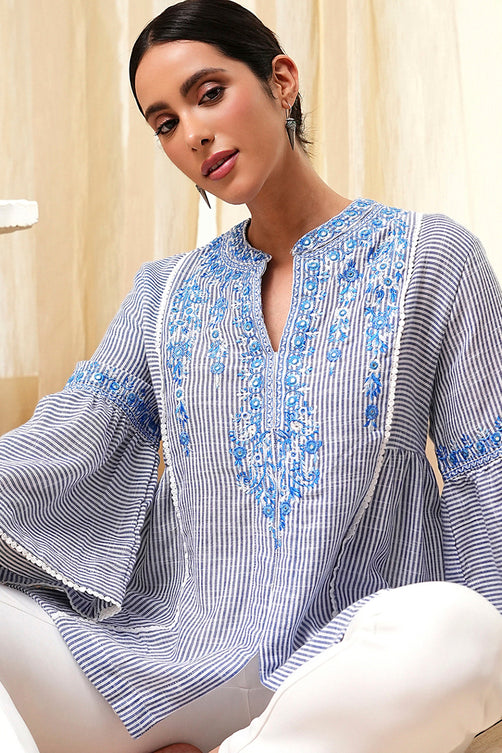 Woman wearing a blue and white embroidered top sitting on a couch.