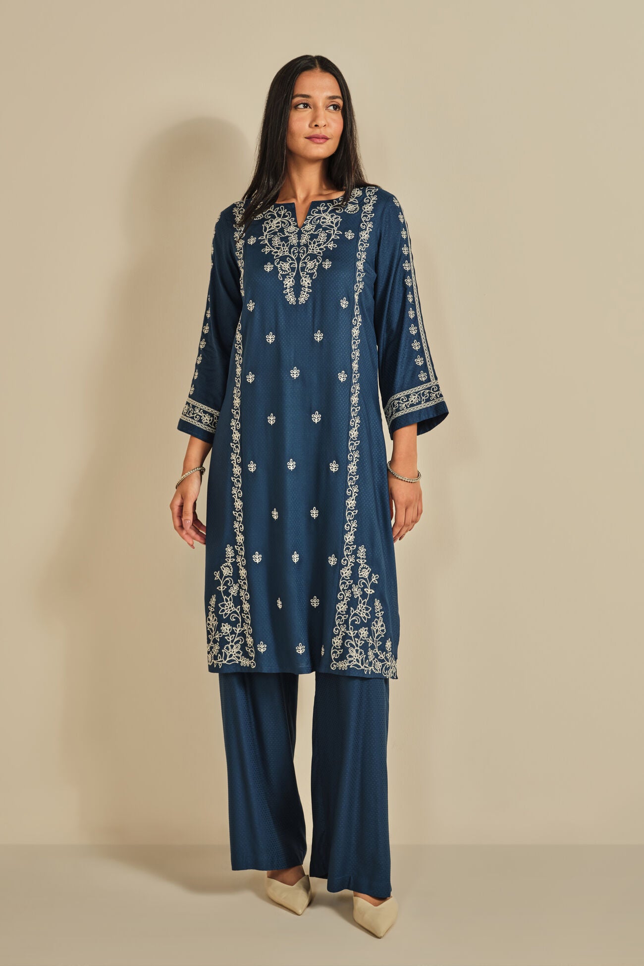 Woman wearing a blue embroidered outfit on a beige background