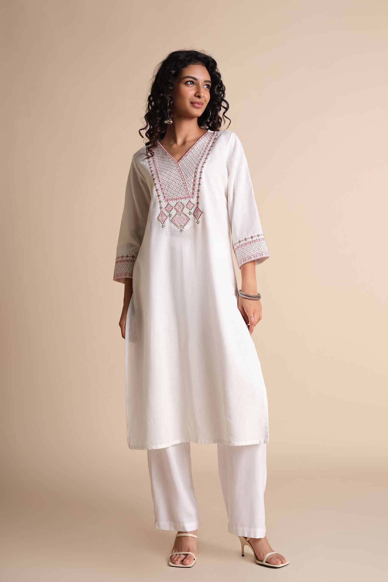 Woman wearing a white kurta with intricate embroidery on a beige background