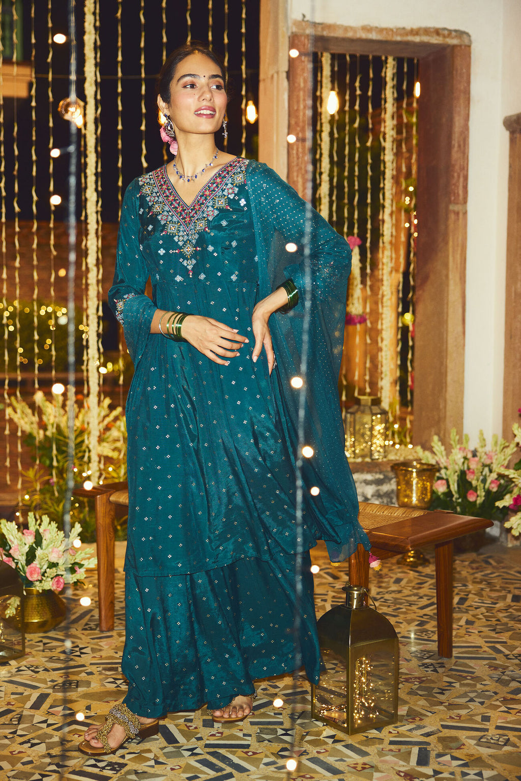 Woman in a teal saree with floral decorations and lights in the background